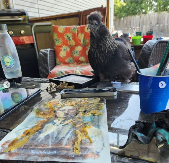 Sara Leger Painting outside with a silkie chicken sitting on the table